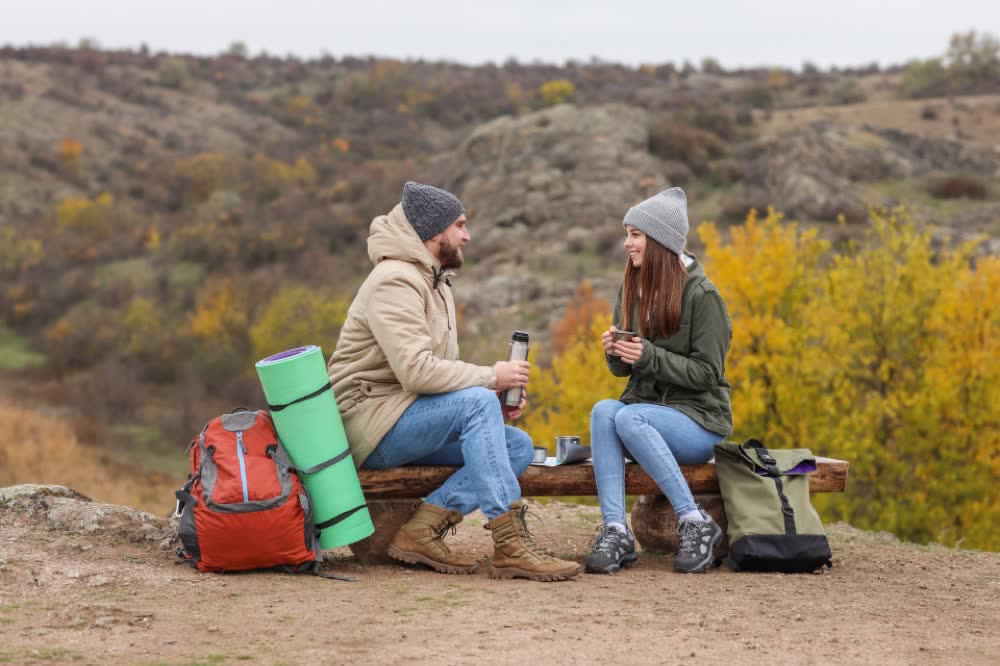 Two walkers sharing a laugh and a hot drink on a trail bench