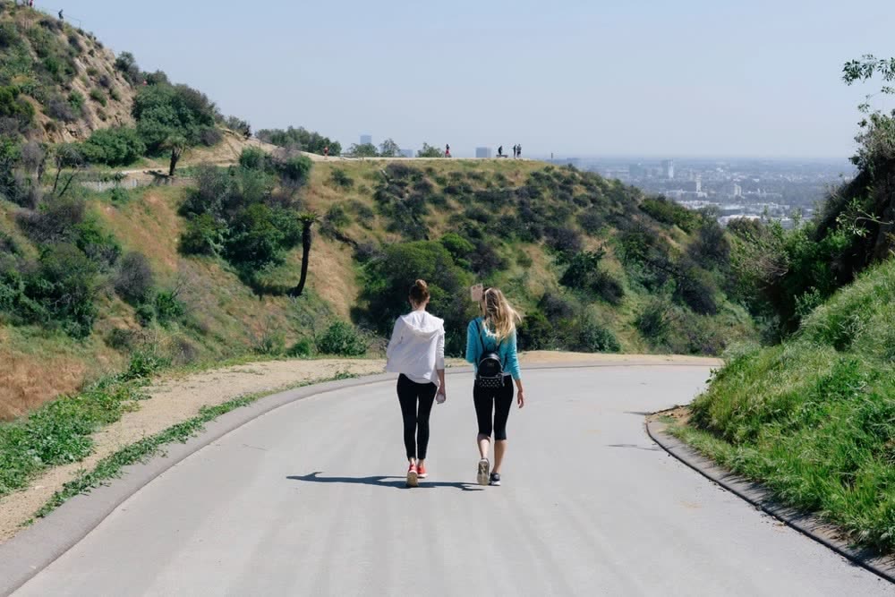 Two friends walking side by side up a paved hill road